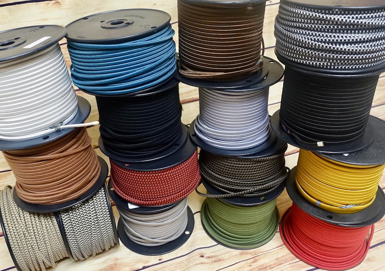 May include: A collection of spools of colorful electrical cord, including black, white, brown, red, yellow, green, blue, and gray. The cords are wound around spools with black plastic bases.
