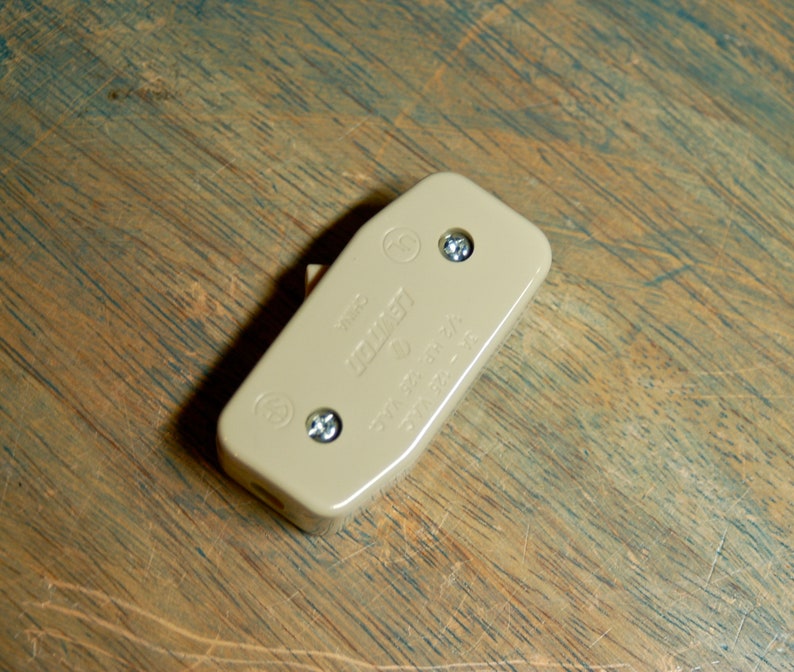 May include: A beige plastic electrical outlet cover with two screws and the text "125V 15A 60Hz" printed on it.