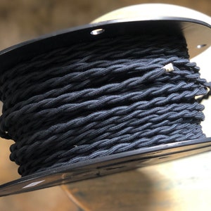 May include: A spool of black twisted electrical cord. The cord is wound around a black plastic spool.