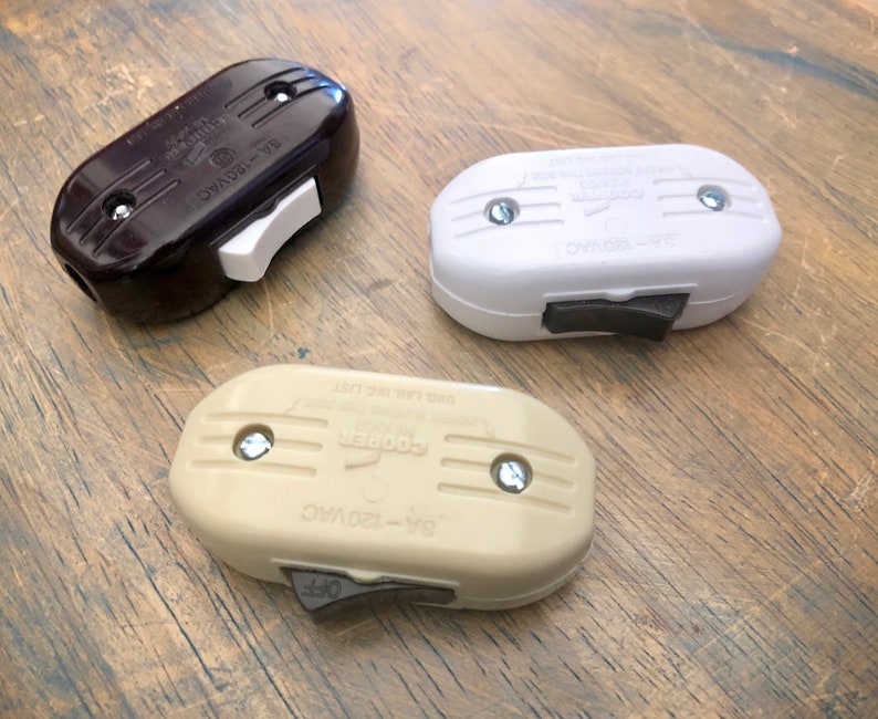 Puede incluir: Tres interruptores de luz vintage en marr&oacute;n, blanco y beige. Cada interruptor tiene una palanca de palanca y est&aacute; etiquetado como "6A-120VAC".