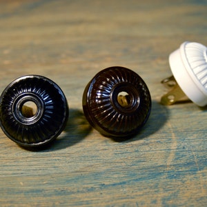 Puede incluir: Tres tapas de interruptor de luz vintage, una blanca, una negra y una marrón. Las tapas tienen un diseño decorativo y acanalado.