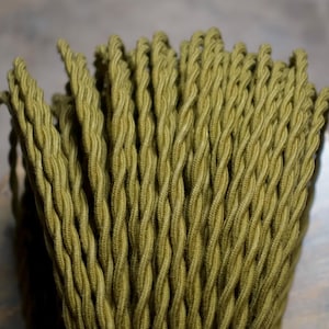 Peut inclure: Gros plan sur un faisceau de cordons en tissu torsadé vert olive. Les cordons sont tissés serrés, créant une surface texturée. Les cordons sont probablement destinés au câblage électrique ou à des fins décoratives.