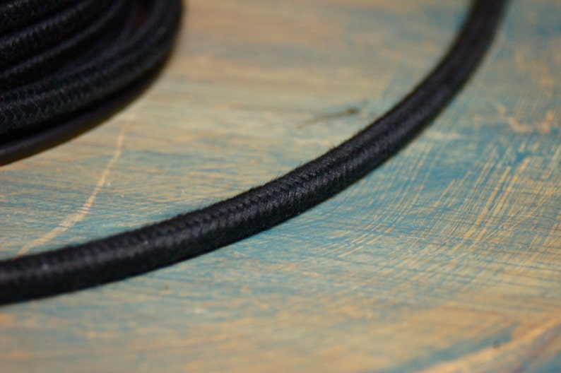 May include: Close-up of black electrical cord with a braided fabric covering. The cord is lying on a blue and brown wooden surface.