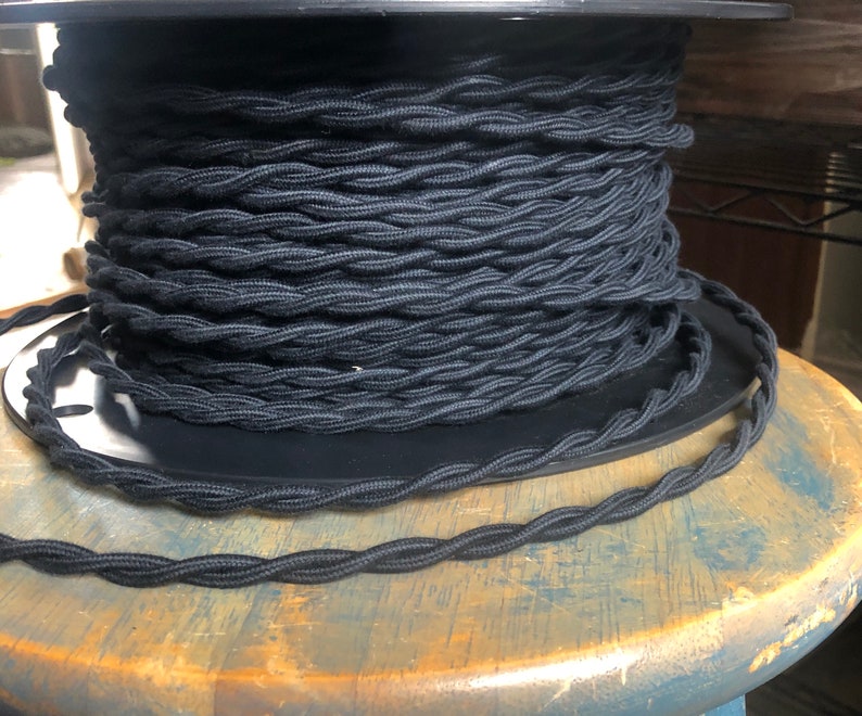 May include: A spool of black braided electrical cord. The cord is wound tightly around the spool and is ready to be used for electrical projects.