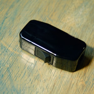 May include: A black toggle switch with a shiny finish. The switch is rectangular and has a small, black lever on the side.