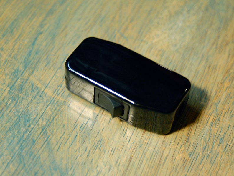 May include: A black toggle switch with a shiny finish. The switch is rectangular and has a small, black lever on the side.