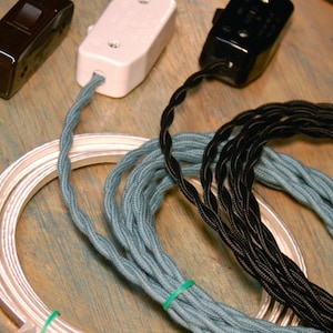 May include: Three spools of electrical cord, one silver, one blue, and one black. The cords are coiled and ready to be used for electrical projects.