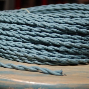 Peut inclure: Gros plan d'une bobine de cordon en tissu torsadé bleu sarcelle. Le cordon est enroulé serré et a une surface lisse et texturée.