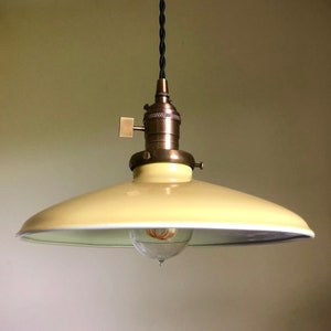 May include: A yellow pendant light with a white rim and a brass socket. The light is hanging from a black cord.