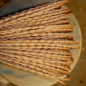 May include: A close-up of a spool of gold braided electrical cord. The cord is tightly wound and has a shiny, metallic finish.