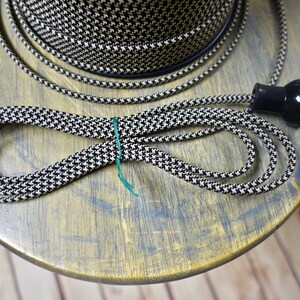 May include: Black and white houndstooth patterned electrical cord with a black plug. A spool of matching cord is visible in the background. The cord is looped and secured with a green tie, suggesting a craft or DIY project.