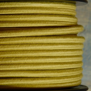 Puede incluir: Una bobina de cable eléctrico amarillo. El cable está enrollado firmemente alrededor de la bobina y está listo para ser utilizado en proyectos eléctricos.