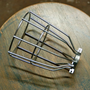 Puede incluir: Una pantalla de bombilla de jaula de metal plateado con una parte superior redondeada y un marco de alambre.