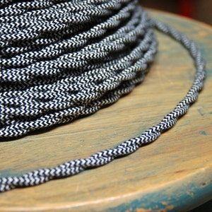 Puede incluir: Una bobina de cable eléctrico con estampado en blanco y negro. El cable está enrollado apretado y tiene un patrón en zigzag.