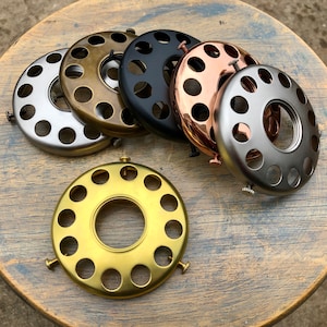 Puede incluir: Surtido de anillos para pantallas de lámparas de metal en varios acabados, incluyendo plata, oro, negro y cobre. Los anillos tienen forma circular con múltiples agujeros alrededor del borde.
