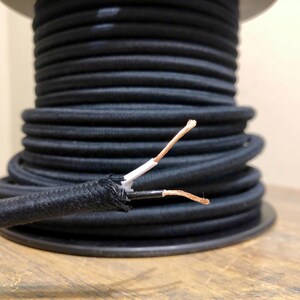 May include: Close-up of black electrical cord with exposed copper wire ends. The cord is wound around a spool.