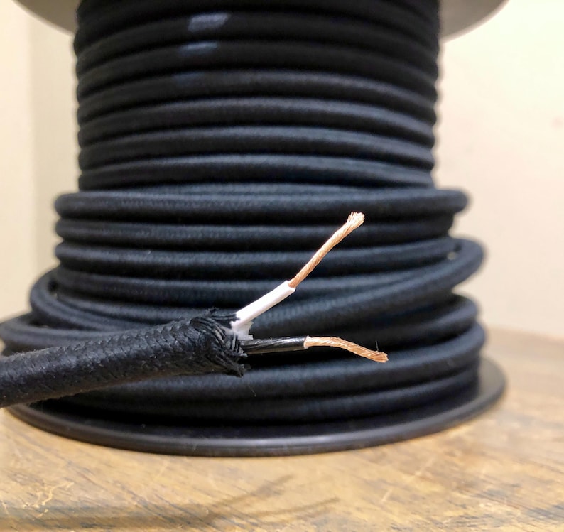 May include: Close-up of black electrical cord with exposed copper wire ends. The cord is wound around a spool.