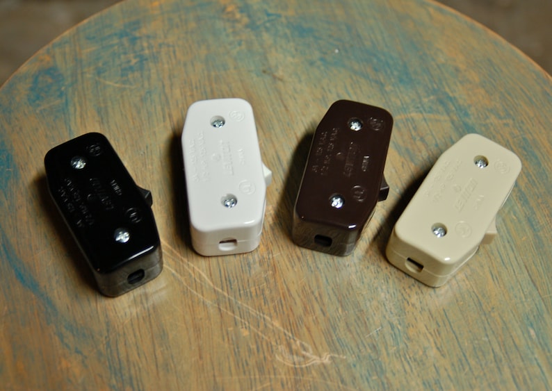 May include: Four toggle switches in black, white, brown, and beige. The switches are all the same size and shape, and they have two screws on each side. The switches are all in focus.