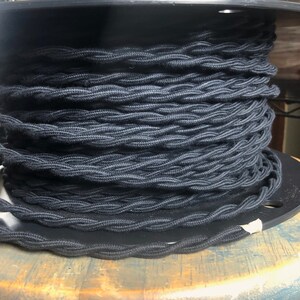 May include: A spool of black braided electrical cord. The cord is wound tightly around the spool, creating a thick, textured look.