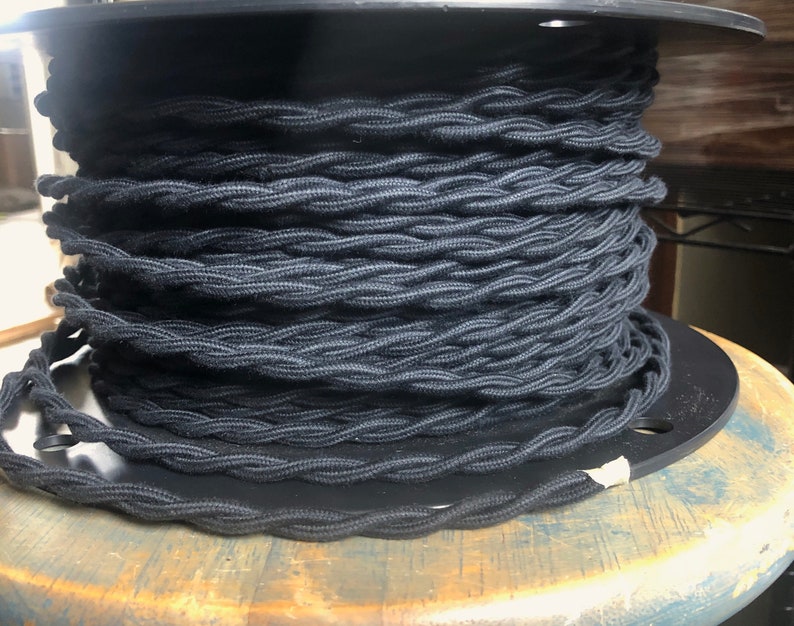 May include: A spool of black braided electrical cord. The cord is wound tightly around the spool, creating a thick, textured look.