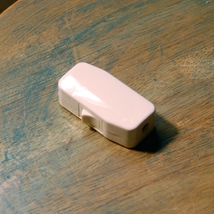 May include: A white plastic inline switch with a rocker switch. The switch is on a wooden surface.