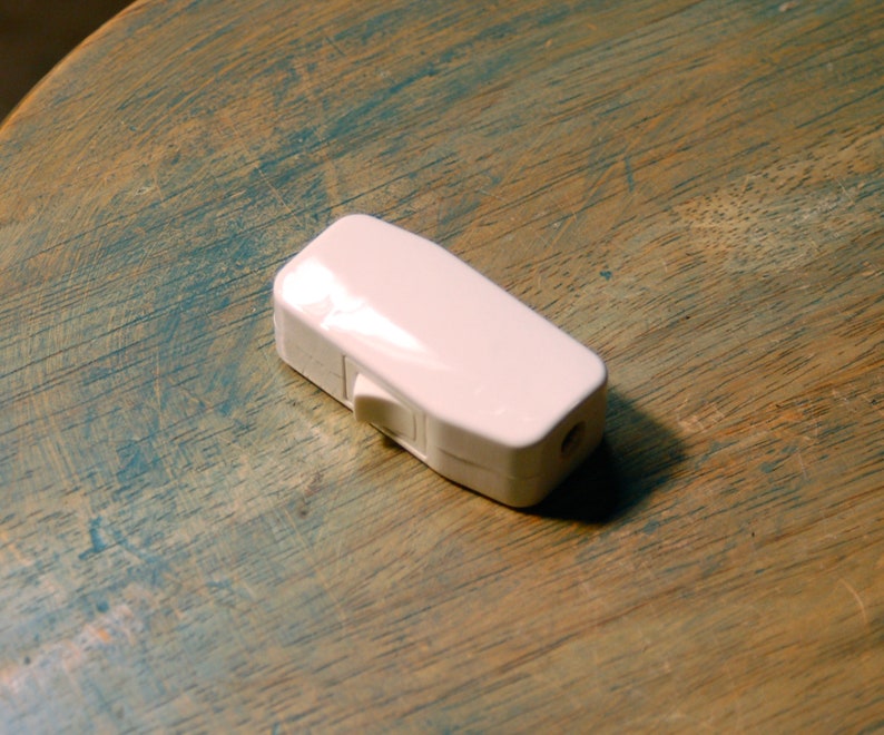 May include: A white plastic inline switch with a rocker switch. The switch is on a wooden surface.