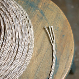 Peut inclure: Une bobine de cordon électrique tressé argenté et beige. Le cordon est torsadé et a un aspect métallique.