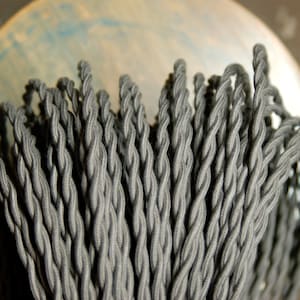 May include: Close-up of a bundle of gray twisted electrical cord. The cord is made of a braided fabric material.