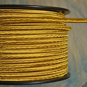 May include: A spool of gold cord with a black plastic spool. The cord is tightly wound and has a ribbed texture.