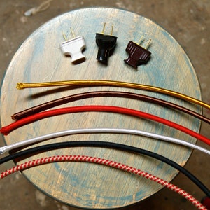 May include: Assortment of six different colored electrical cords with three different types of plugs. The cords are gold, brown, red, white, black, and red and white checkered.