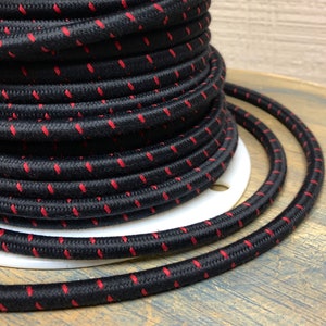 Puede incluir: Primer plano de un cable eléctrico negro con costuras rojas. El cable está enrollado alrededor de un carrete.