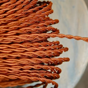 Könnte beinhalten: Nahaufnahme einer Spule mit orangefarbenem geflochtenem Stromkabel. Das Kabel ist gedreht und texturiert und erzeugt einen einzigartigen und dekorativen Look.