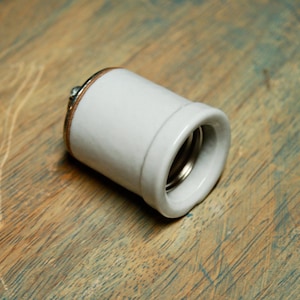 May include: A white ceramic light bulb socket with a copper coloured rim.
