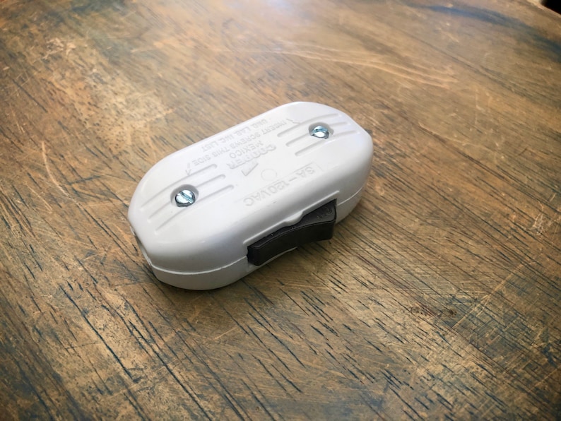Puede incluir: Un interruptor en l&iacute;nea de pl&aacute;stico blanco con un interruptor de palanca negro. El interruptor tiene dos tornillos y el texto "ON/OFF - 6/15A 125V" impreso en el lateral.