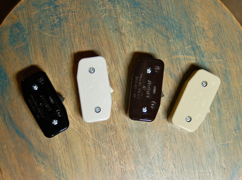May include: Four light switch toggles in different colors: black, white, brown, and beige. The switches are rectangular and have a small lever on the side.