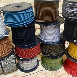 May include: A collection of spools of colorful electrical cord, including black, white, brown, red, yellow, green, blue, and gray. The cords are wound around spools with black plastic bases.