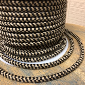 Puede incluir: Primer plano de un carrete de cable eléctrico estampado en negro y marrón. El cable está enrollado firmemente alrededor del carrete y tiene un patrón de pata de gallo.