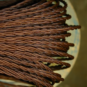 Op de afbeelding: Close-up van een spoel met bruin gevlochten elektriciteitsdraad. De draad is strak gewikkeld en heeft een glad, getextureerd oppervlak.