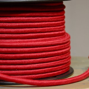 Puede incluir: Un carrete de cable eléctrico rojo, enrollado de forma compacta y listo para ser utilizado en una variedad de proyectos.