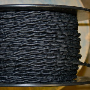 Peut inclure: Une bobine de cordon électrique tressé noir. Le cordon est enroulé serré autour de la bobine, créant un motif texturé.
