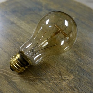 May include: A clear glass light bulb with a gold metal base. The bulb has a traditional filament design.