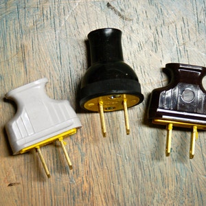 May include: Three electrical plugs with different colored plastic housings: white, black, and brown. The plugs have two prongs each, and the prongs are gold colored.