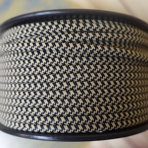 May include: A spool of beige and black patterned rope. The rope is tightly wound around a black plastic spool. The pattern is a small, repeating houndstooth design. The rope appears to be made of a durable material.
