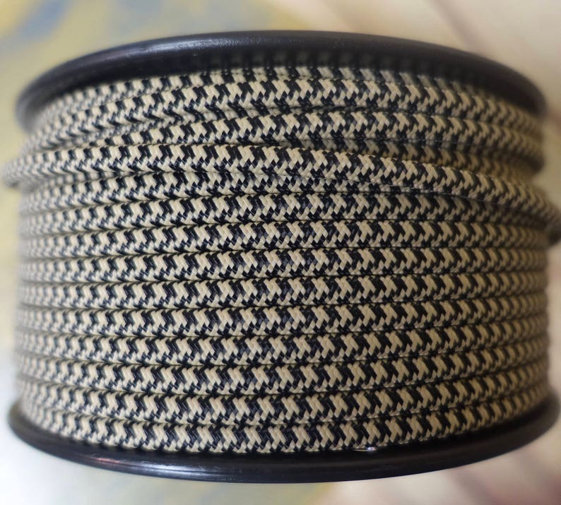 May include: A spool of beige and black patterned rope. The rope is tightly wound around a black plastic spool. The pattern is a small, repeating houndstooth design. The rope appears to be made of a durable material.