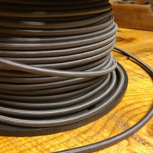 May include: A spool of silver gray braided cord, wound tightly around a black plastic spool. The cord is smooth and has a subtle sheen.