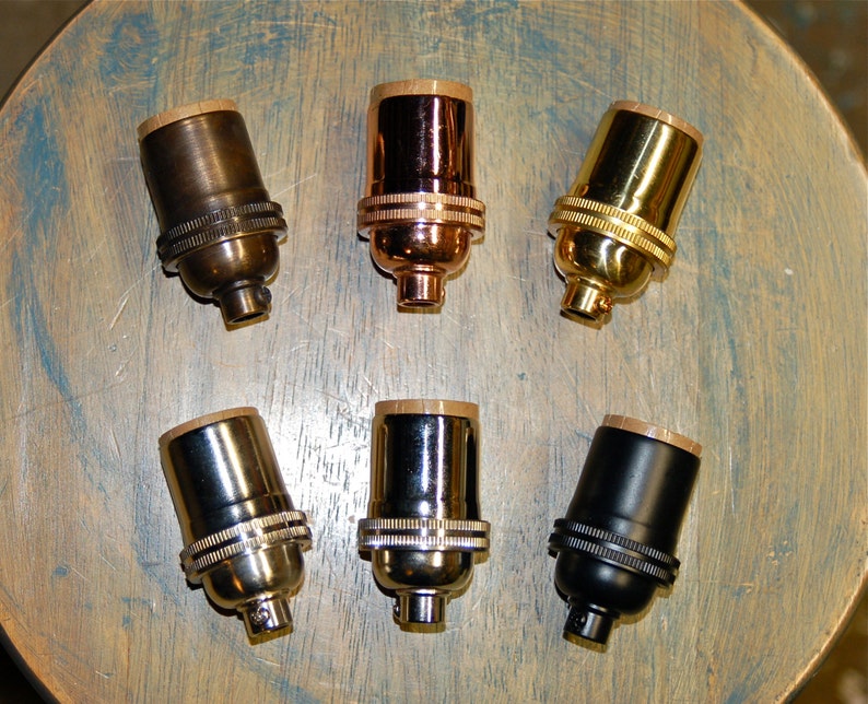 May include: Six different colored light bulb sockets. The sockets are made of metal and have a brass finish. The sockets are arranged in a circle on a wooden surface.