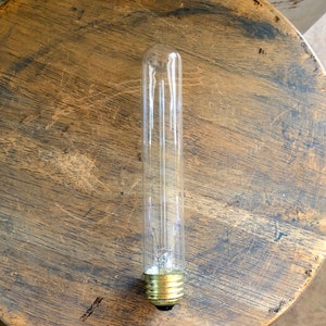 May include: A clear glass light bulb with a standard screw-in base. The bulb is long and thin, with a frosted finish.