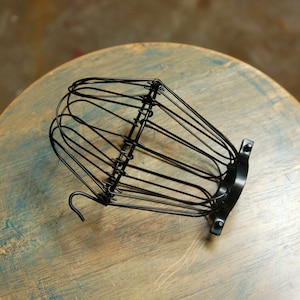 May include: Black metal cage light shade with a rounded top and a hook on the side.