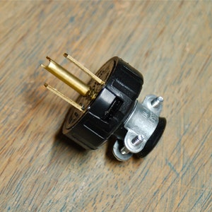 Könnte beinhalten: Ein schwarzer Stecker mit einem goldfarbenen Mittelkontakt und drei Stiften. Der Stecker hat ein schwarzes Gummigehäuse und einen silbernen Metallanschluss.