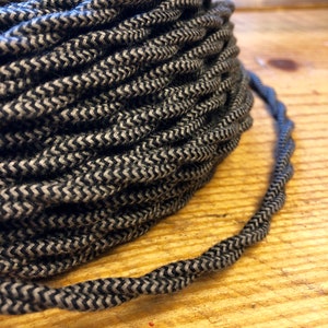 May include: Close-up of a spool of black and white braided fabric electrical cord. The cord is twisted and has a chevron pattern.